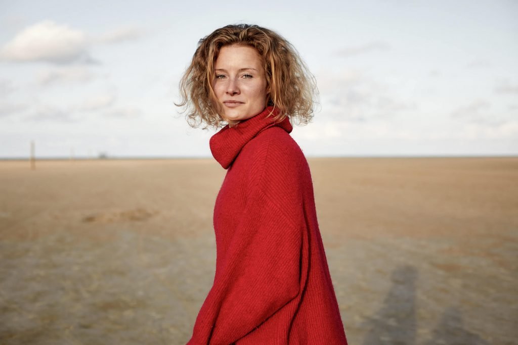 Sandra Mühmel-Yogamodel am Strand bei Sonnenaufgang im roten Pullover